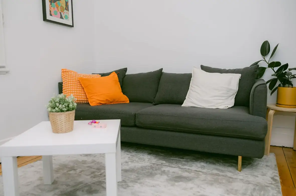 A warm, comfortable counselling room with a grey sofa, orange cushions and indoor plants