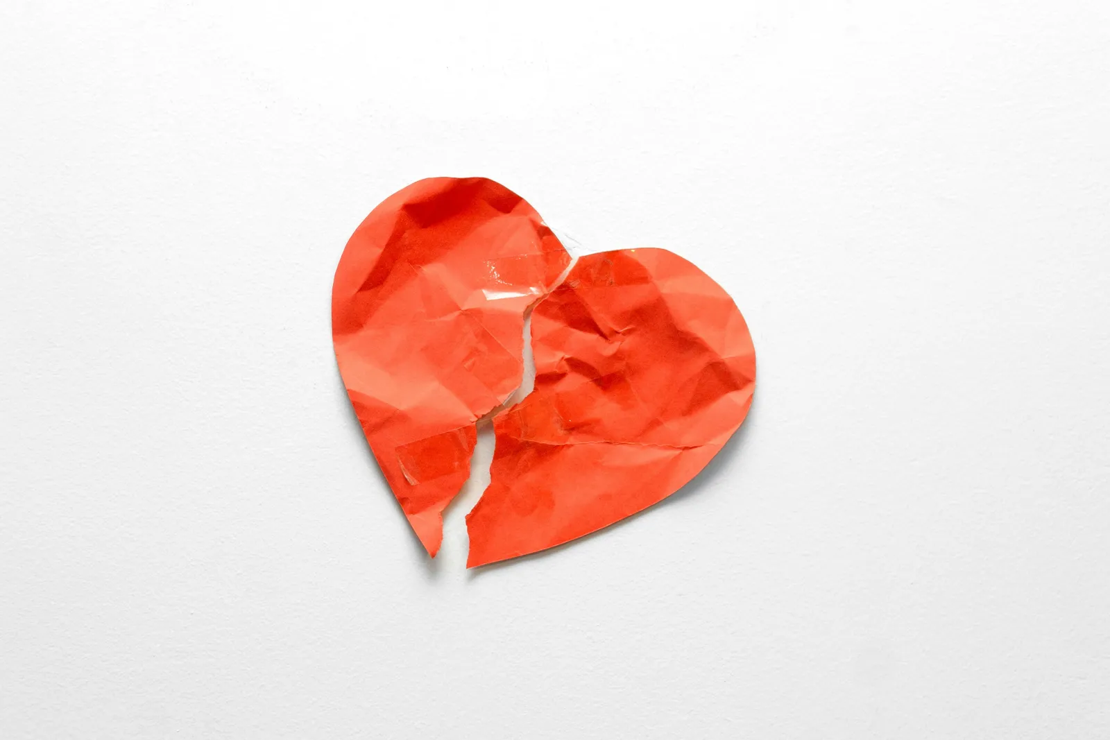 A crumpled red paper heart, torn down the middle, on a white background.