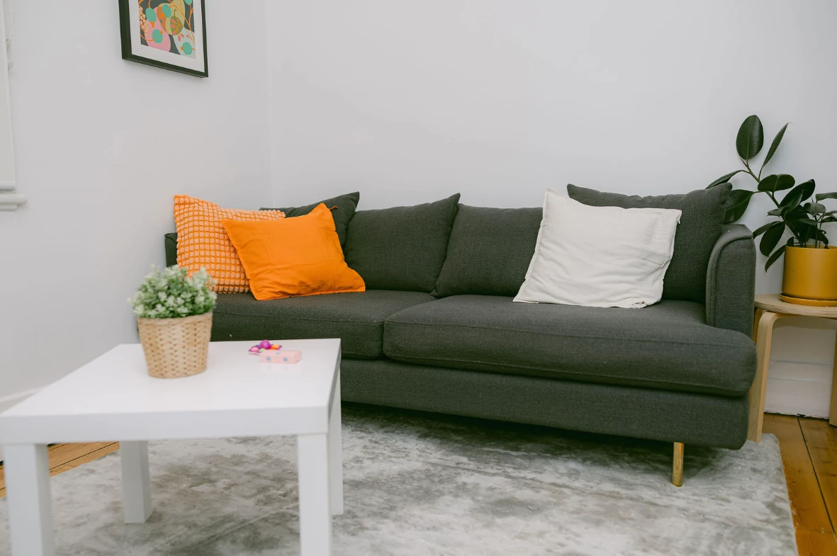 A warm, comfortable counselling room with a grey sofa, orange cushions and indoor plants